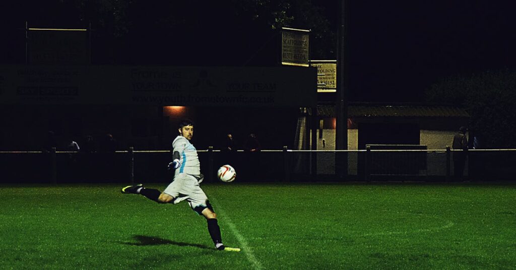 Dynamic action shot of a soccer player kicking the ball during a night game in Somerset, England.